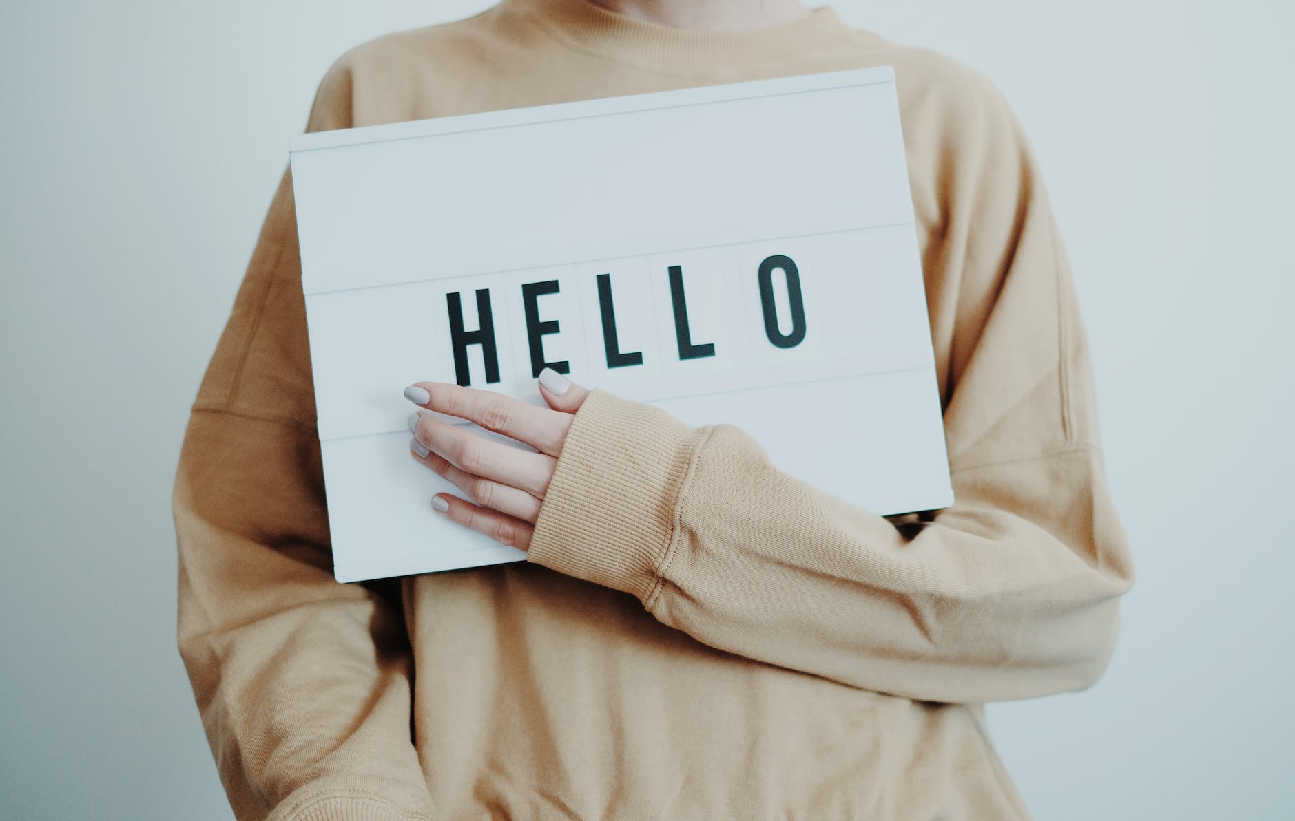 person in beige sweater holding a hello sign